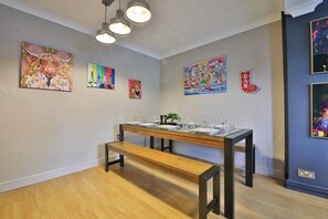 Ein Essbereich mit einem Holztisch, gedeckt für vier Personen, einer Bank und verschiedenen Kunstwerken an den Wänden.