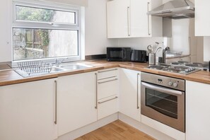 A modern kitchen with white cabinets, a stainless steel oven, a microwave, and a window with a view of greenery. - Stylish 2BR Apartment near Bute Park (Cardiff)
