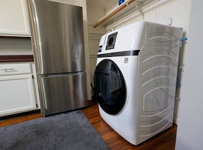 Una cocina compacta con un refrigerador de acero inoxidable, una lavadora integrada y una alfombra gris en el suelo.