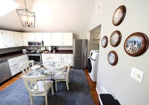 A compact kitchen with white cabinets, a stainless steel refrigerator, and a dining area with a glass table and white chairs.