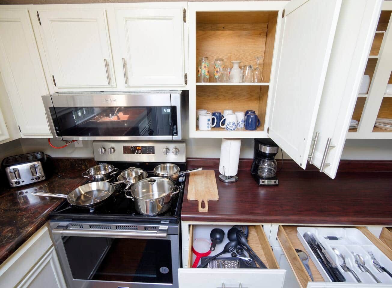 Une cuisine avec des meubles blancs, un four à micro-ondes, une cuisinière et divers ustensiles.