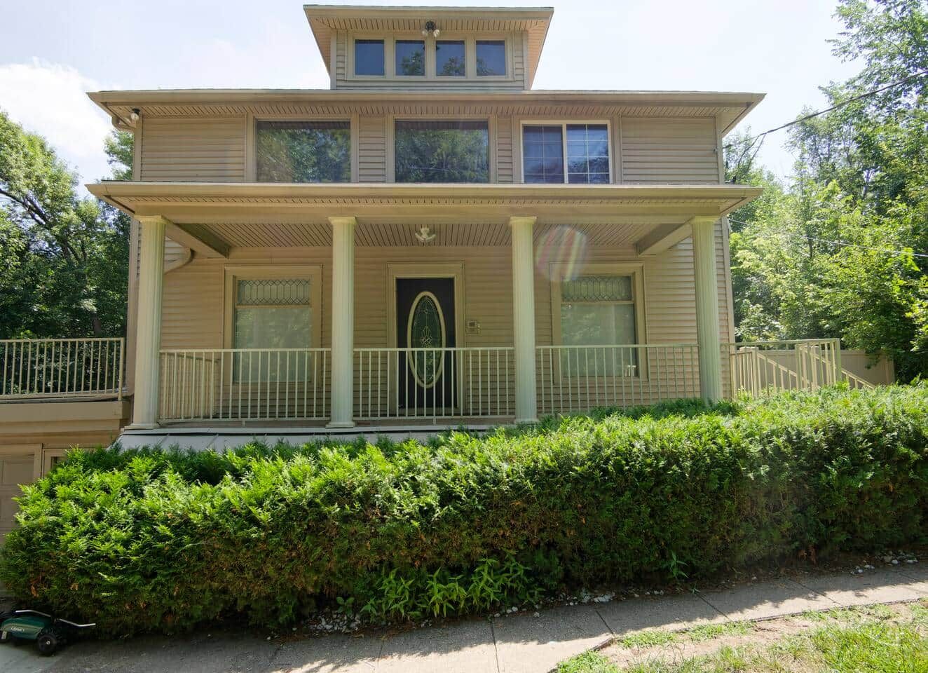 A two-story house with a front porch, a door with an arched window, and a small balcony.
