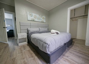 A bedroom with a bed, a nightstand, a wardrobe, and a door leading to another room.