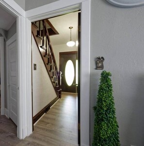 Un pasillo con una escalera de madera, una puerta y un teléfono instalado en la pared.