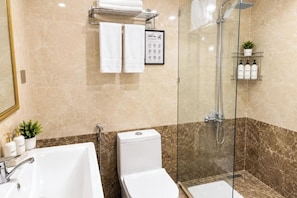 Une salle de bain moderne avec une douche à parois de verre, un lavabo blanc et des toilettes. Des serviettes sont suspendues sur un porte-serviettes, et un panneau d’information sur l’hôtel, encadré, est accroché au mur.