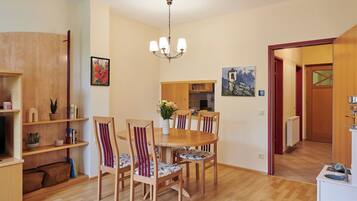 Un comedor con mesa y sillas de madera, una araña y una cocina al fondo.