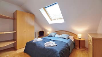 Ein Schlafzimmer mit Dachfenster, einem Bett mit blauer Bettwäsche, Holzmöbeln und einem kleinen Nachttisch mit Lampe.