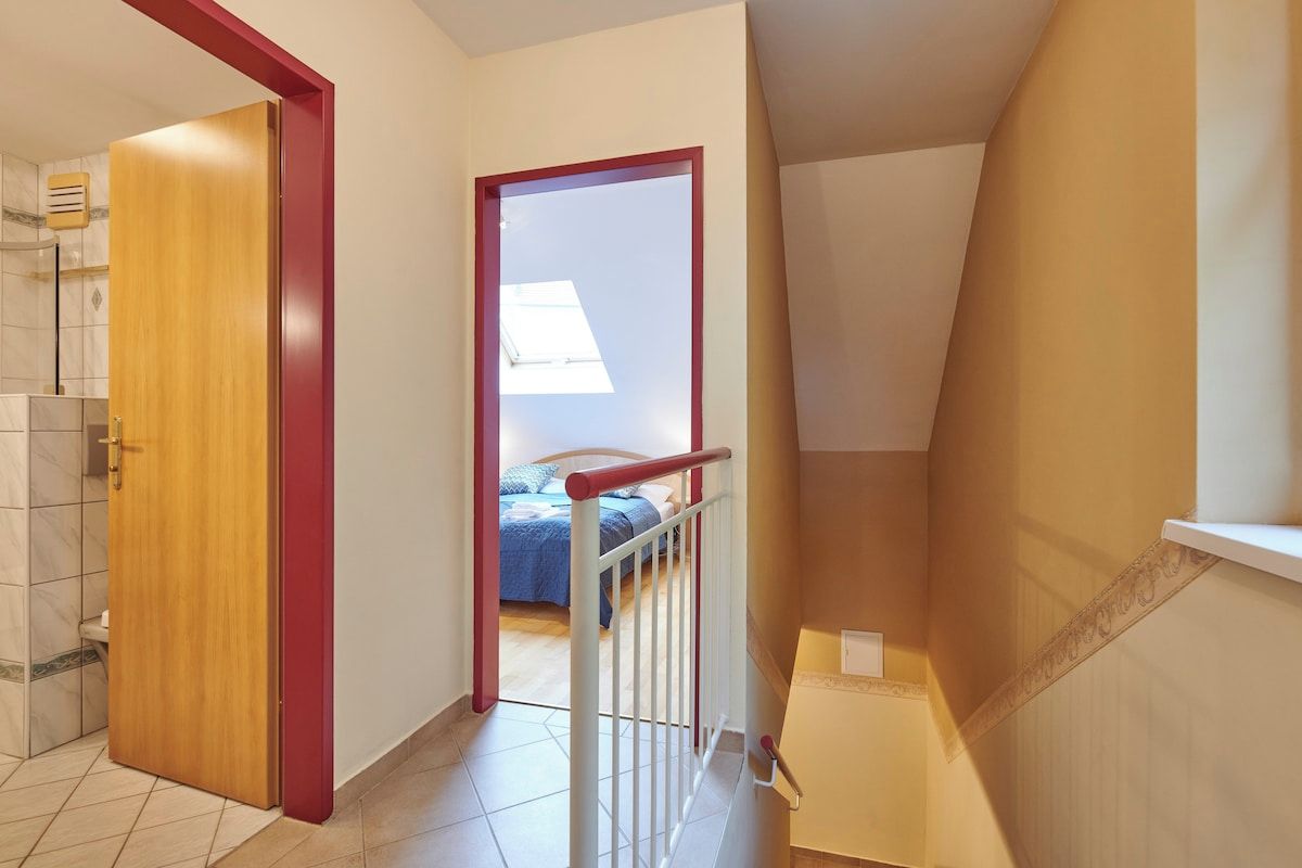 Una habitación con puerta de madera, barandal blanco y cama con cubrecama azul.