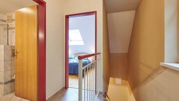 Una habitación con puerta de madera, barandal blanco y cama con cubrecama azul.