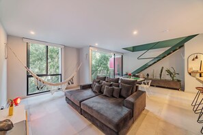 Ein modernes Wohnzimmer mit einem grauen Sofa, einer Hängematte und einem Essbereich mit Tisch und Stühlen.