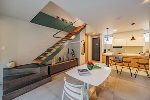 Eine moderne Küche mit einer zentralen Kochinsel, einer Treppe im Grünton mit Holzdekor und einem Essbereich mit weißem Tisch und Stühlen.
