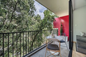 Ein Balkon mit Blick auf Bäume, eine rote Wand und eine Kaktee.
