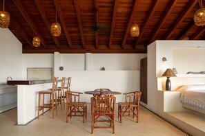A room with a wooden ceiling, a dining table with chairs, a bed with a lamp, and a wall-mounted light fixture. - Casa Privada Frente al Mar | Lujo, Playa y Exclusi (Troncones)