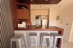 A modern kitchen with a wooden countertop, a microwave, a refrigerator, and a sink. There are three bar stools and a small plant on the countertop. - Torre San Isidro by Domus Travels (Santiago)