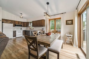 A modern kitchen with wooden cabinets, a dining table with chairs, and a large window providing natural light. - 4BR 2BA, sleeps 8 Near ISU (Ames)