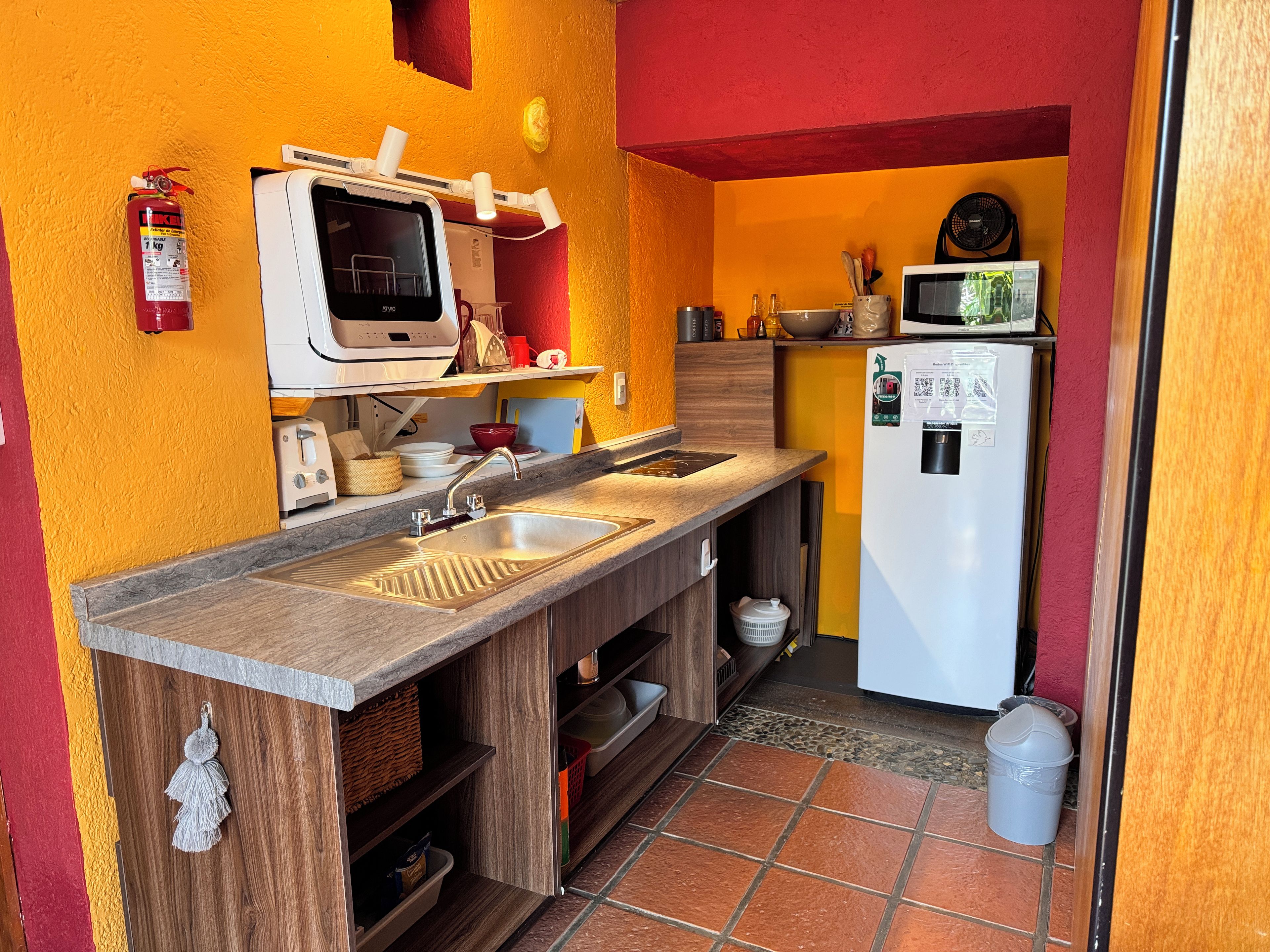 A compact kitchen with a microwave, sink, and a fire extinguisher.