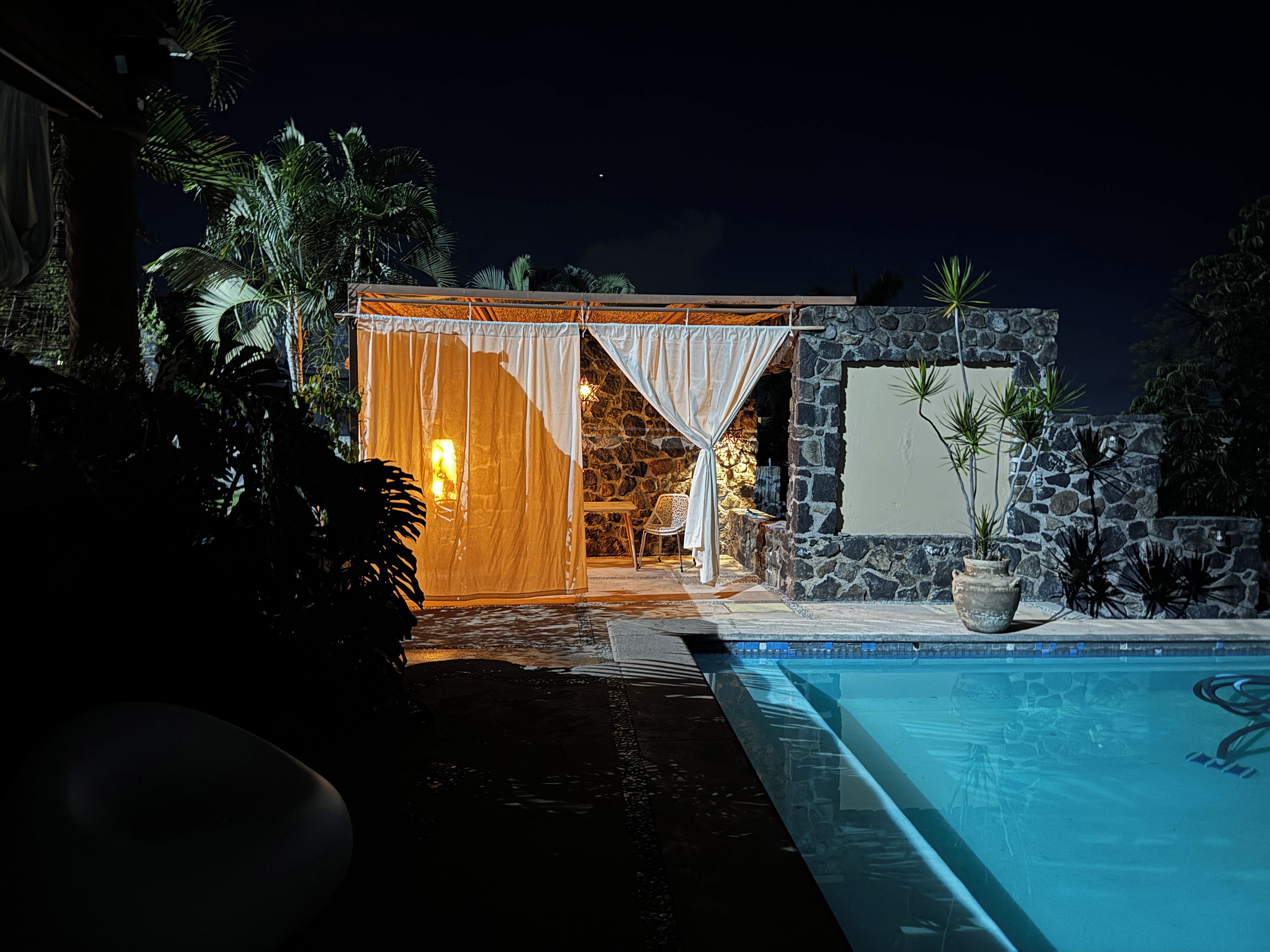 Un complexe hôtelier ouvert la nuit, doté d’une piscine, d’un mur en pierre et d’un espace salon abrité.