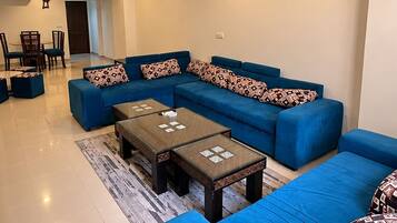 A living room with a sectional sofa, two coffee tables, and a dining area with chairs and a table.