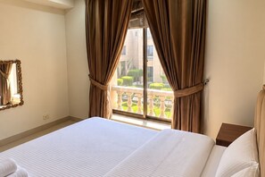 Quarto de hotel com uma cama grande, cortinas, uma janela com vista para uma varanda e um espelho na parede.