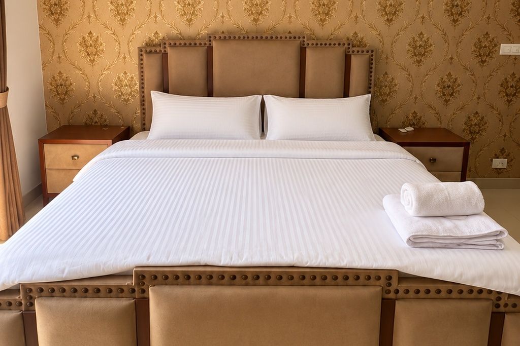 Una cama doble con cabecera, dos mesitas de noche y una toalla doblada sobre la cama.