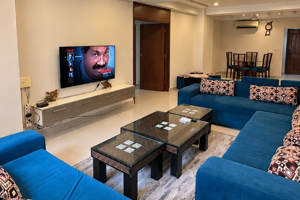 Un salon avec un téléviseur, un canapé bleu, une table basse en verre et un meuble en bois.