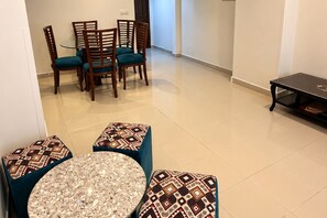 Uma área de refeições com uma mesa redonda e quatro cadeiras, uma mesinha lateral e um banquinho estampado.
