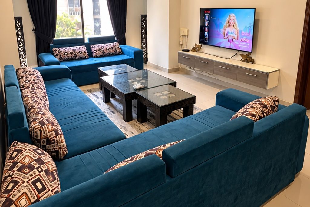 Ein modernes Wohnzimmer mit einem blauen Sofagarnitur, einem Glastisch und einem Flachbildfernseher auf einem weißen Schrank.