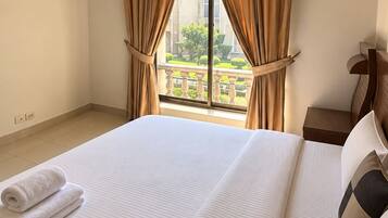 A hotel room with a large bed, a nightstand, and a view of a building and greenery outside.