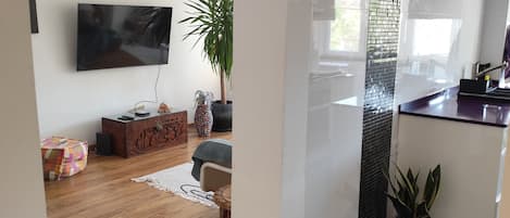 A modern living room with a wooden floor, a flat-screen TV, a potted plant, and a decorative brick wall.