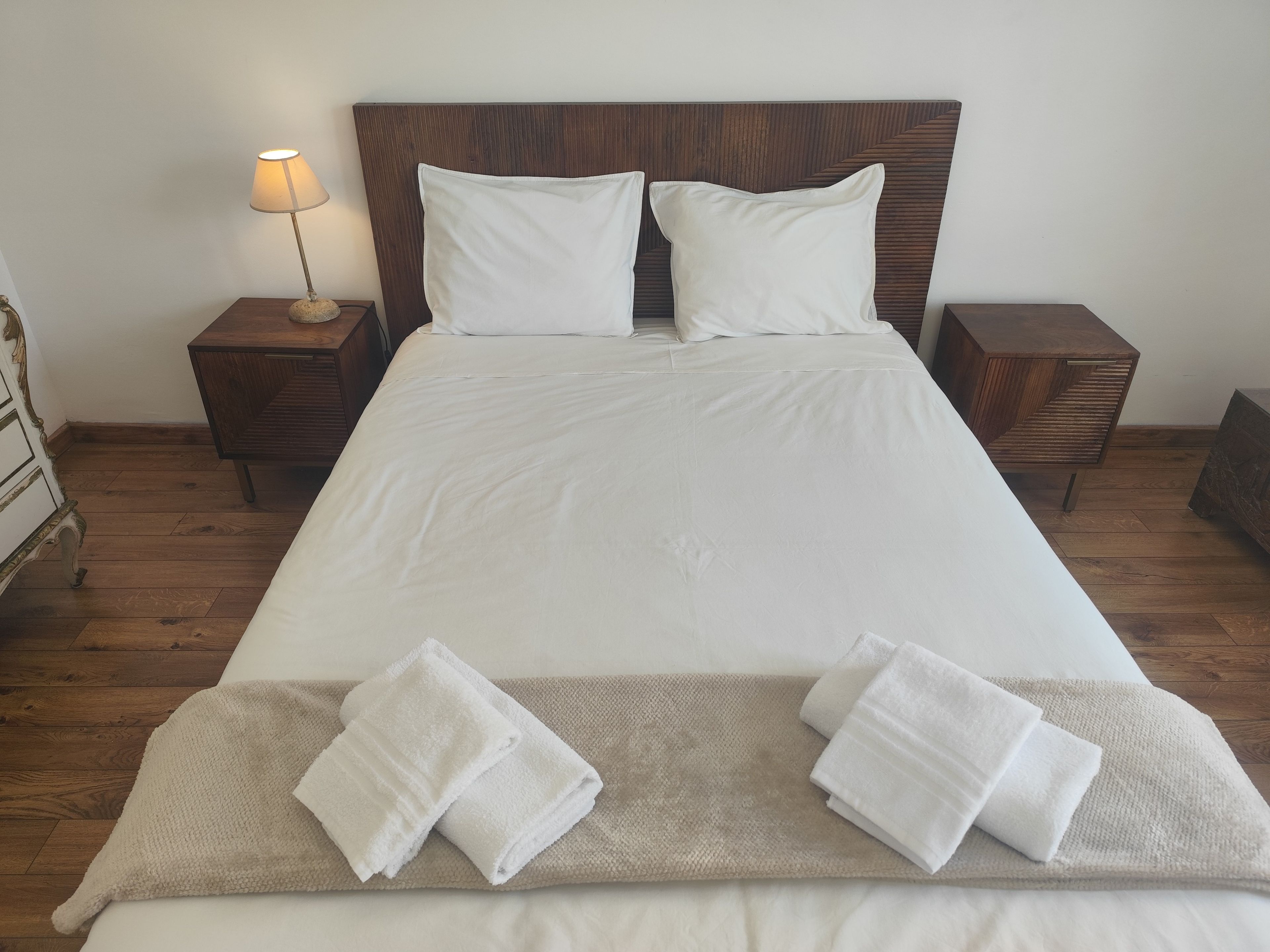 Una cama bien hecha con sábanas blancas, dos almohadas y una manta color beige.