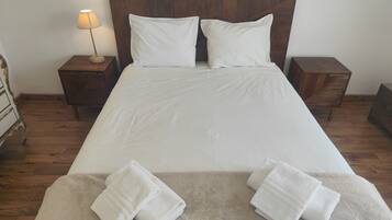 Una cama bien hecha con sábanas blancas, dos almohadas y una manta color beige.