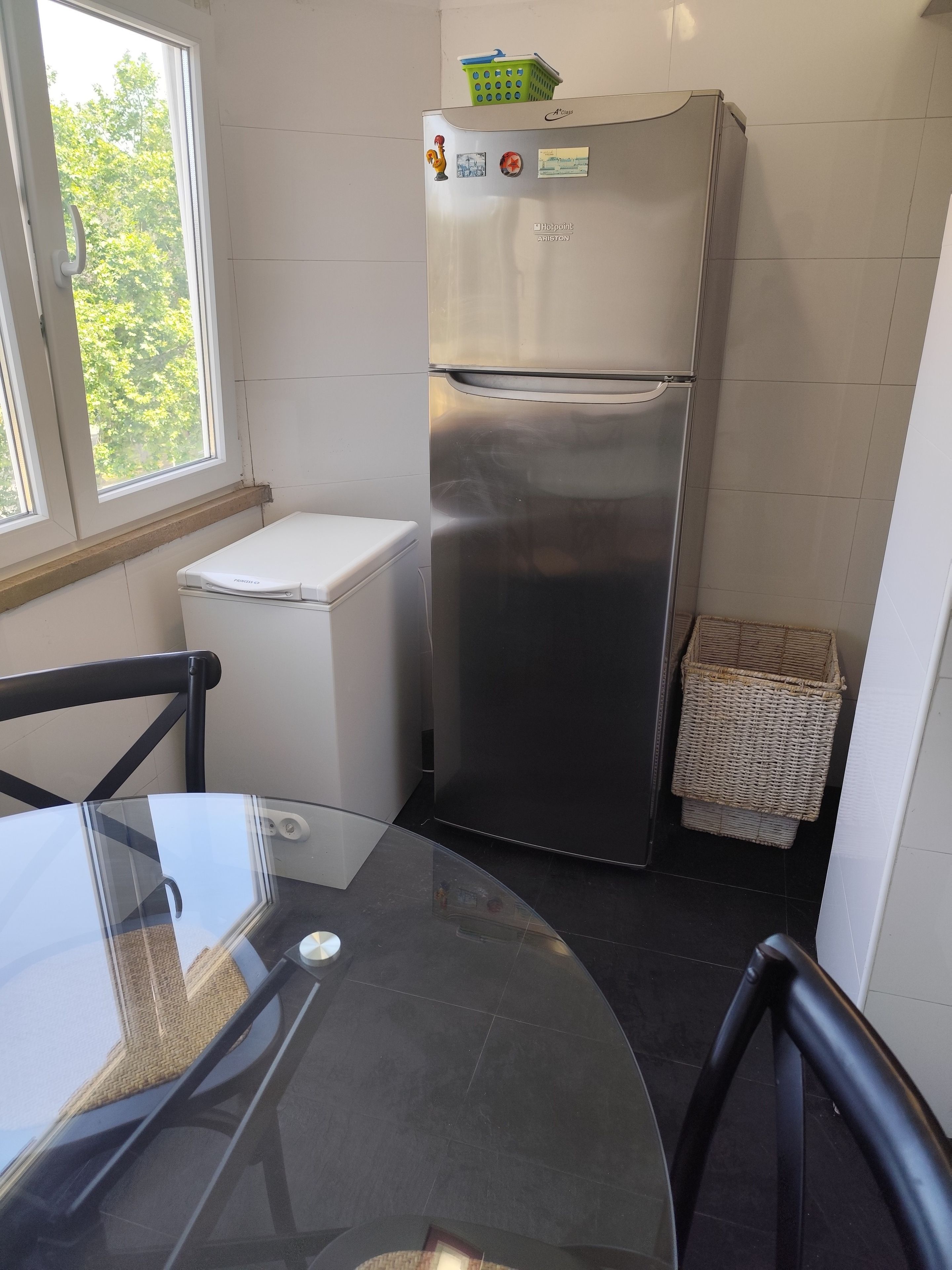 A compact kitchen with a stainless steel refrigerator, a white washing machine, and a glass table.