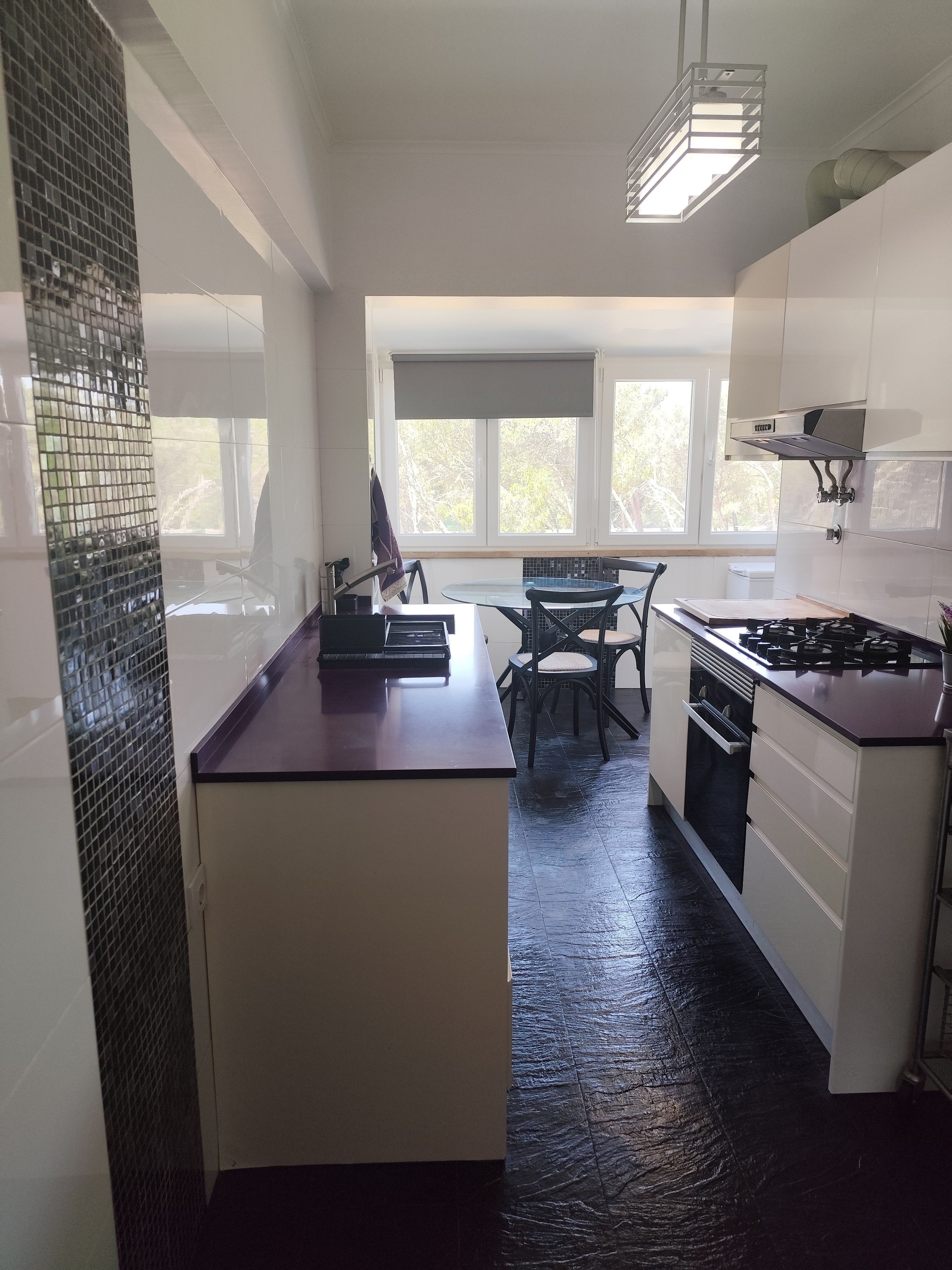 Una cocina moderna con una isla central, un comedor con sillas y ventanas grandes que dejan entrar luz natural.