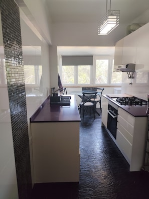 A modern kitchen with a central island, a dining area with chairs, and large windows providing natural light.