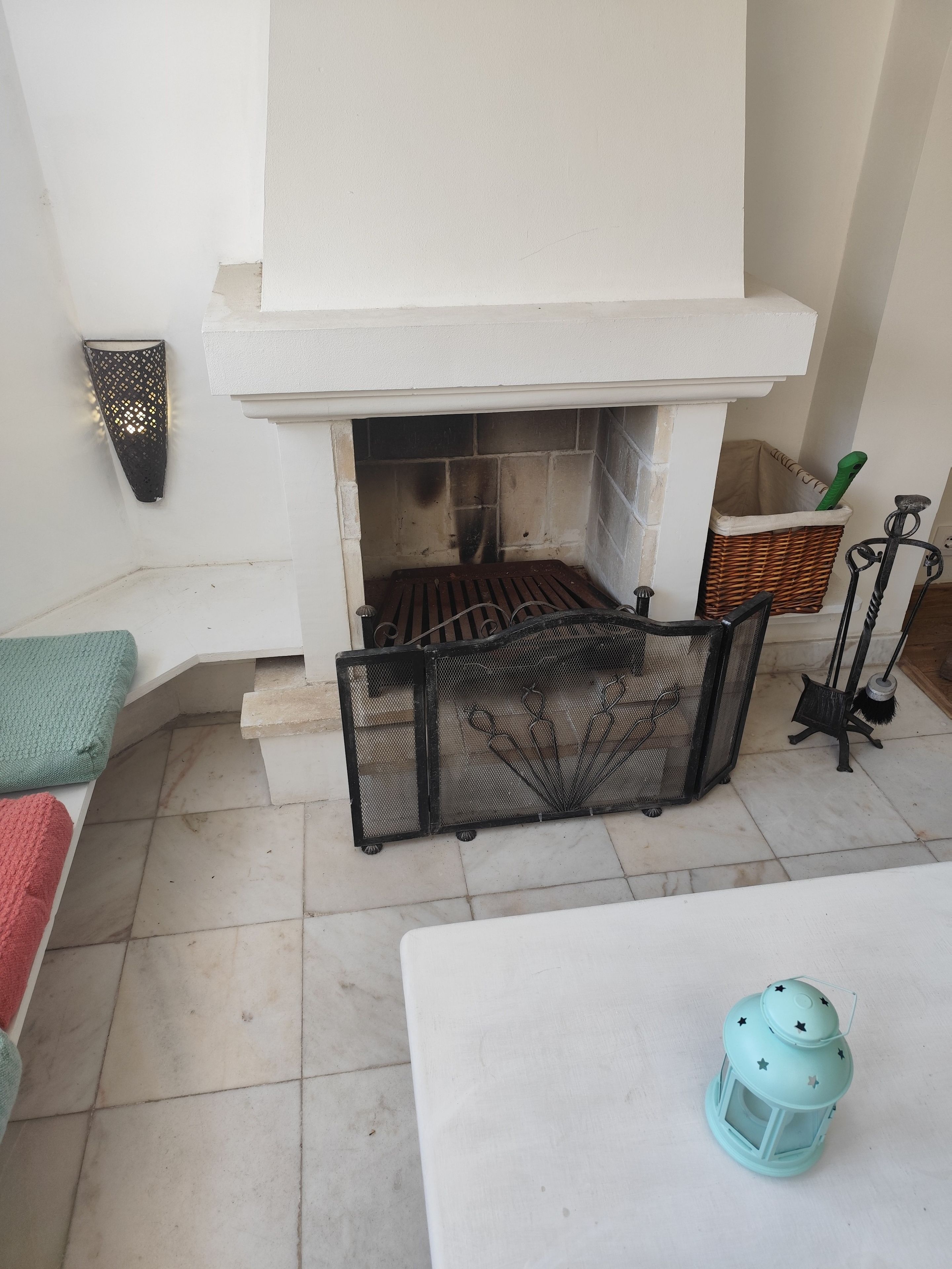 A fireplace with a metal screen, a green lantern, and a wicker basket.
