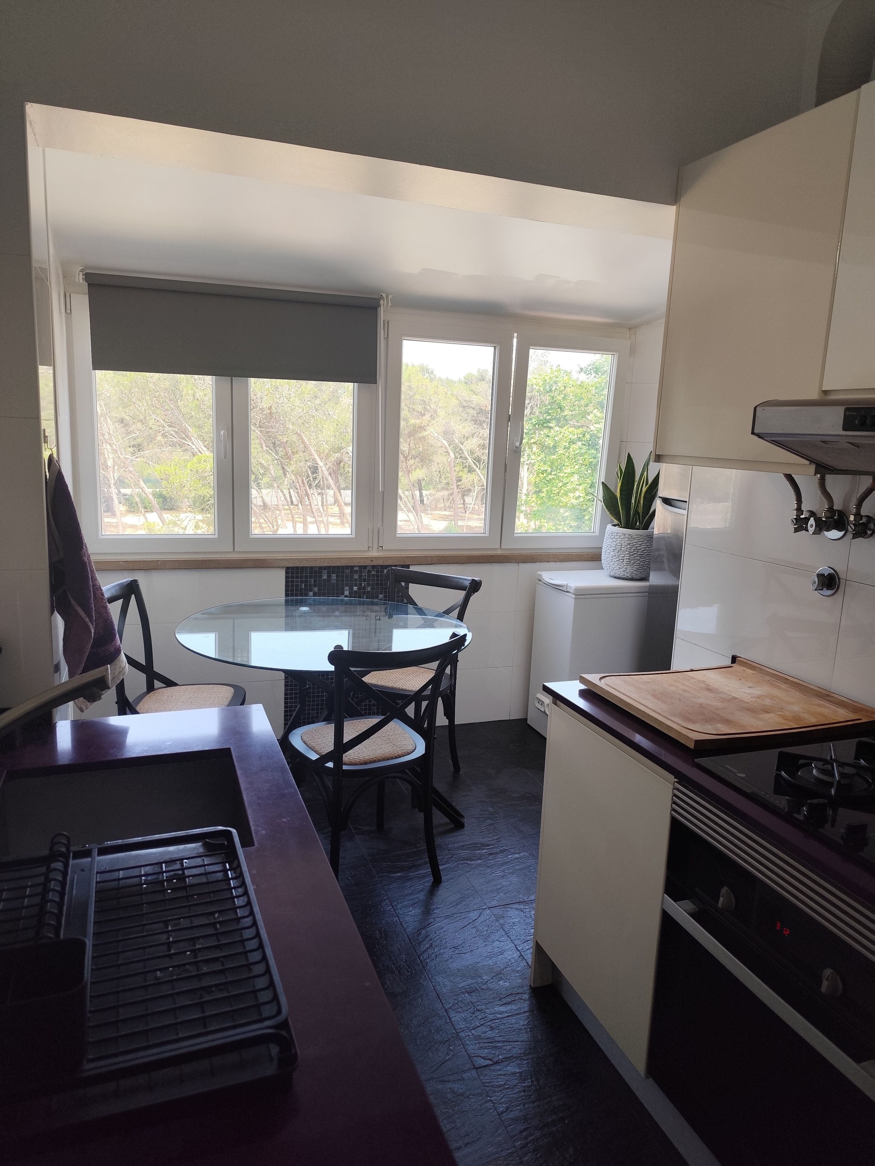 Una cocina con una mesa redonda, sillas, una estufa y un ventanal con vistas a árboles.