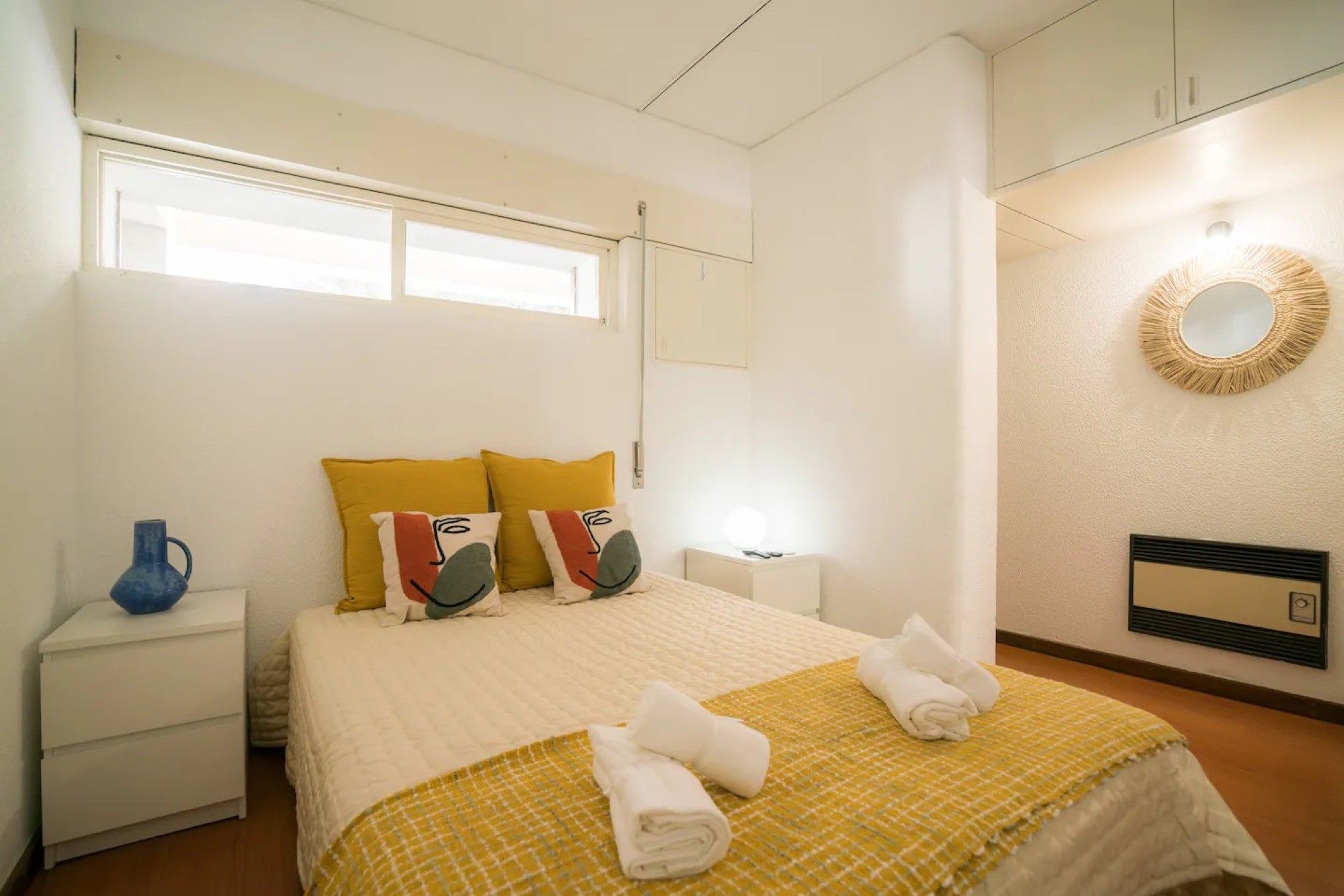 Una habitación de hotel con una cama, una mesita de noche, una lámpara, un espejo y una ventana.