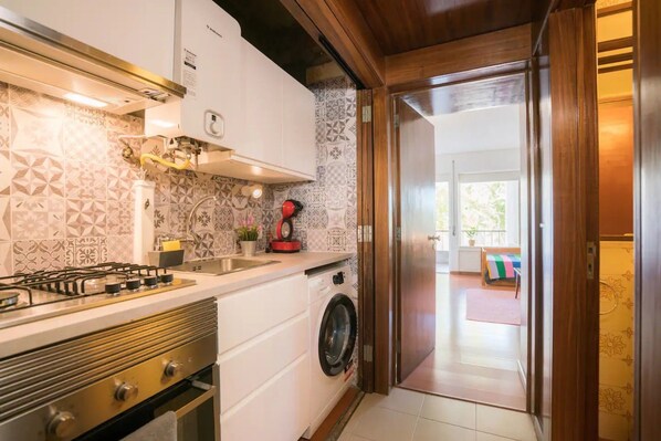 A kitchen with a gas stove, a washing machine, and patterned tiles.