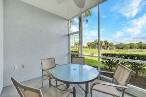 A room with a round glass table and four chairs, large windows with a view of a golf course and trees, and a textured white wall. - Golfer’s Paradise: Turnkey Rental with 24/7 Fitness & Premier Amenities (Naples)