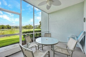 A balcony with a table and chairs, a ceiling fan, and a view of a golf course. - Golfer’s Paradise: Turnkey Rental with 24/7 Fitness & Premier Amenities (Naples)