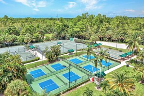 A tennis court complex surrounded by lush greenery and palm trees. - Golfer’s Paradise: Turnkey Rental with 24/7 Fitness & Premier Amenities (Naples)