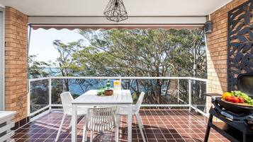 Un balcon avec une table, des chaises, un barbecue et une vue sur la mer.