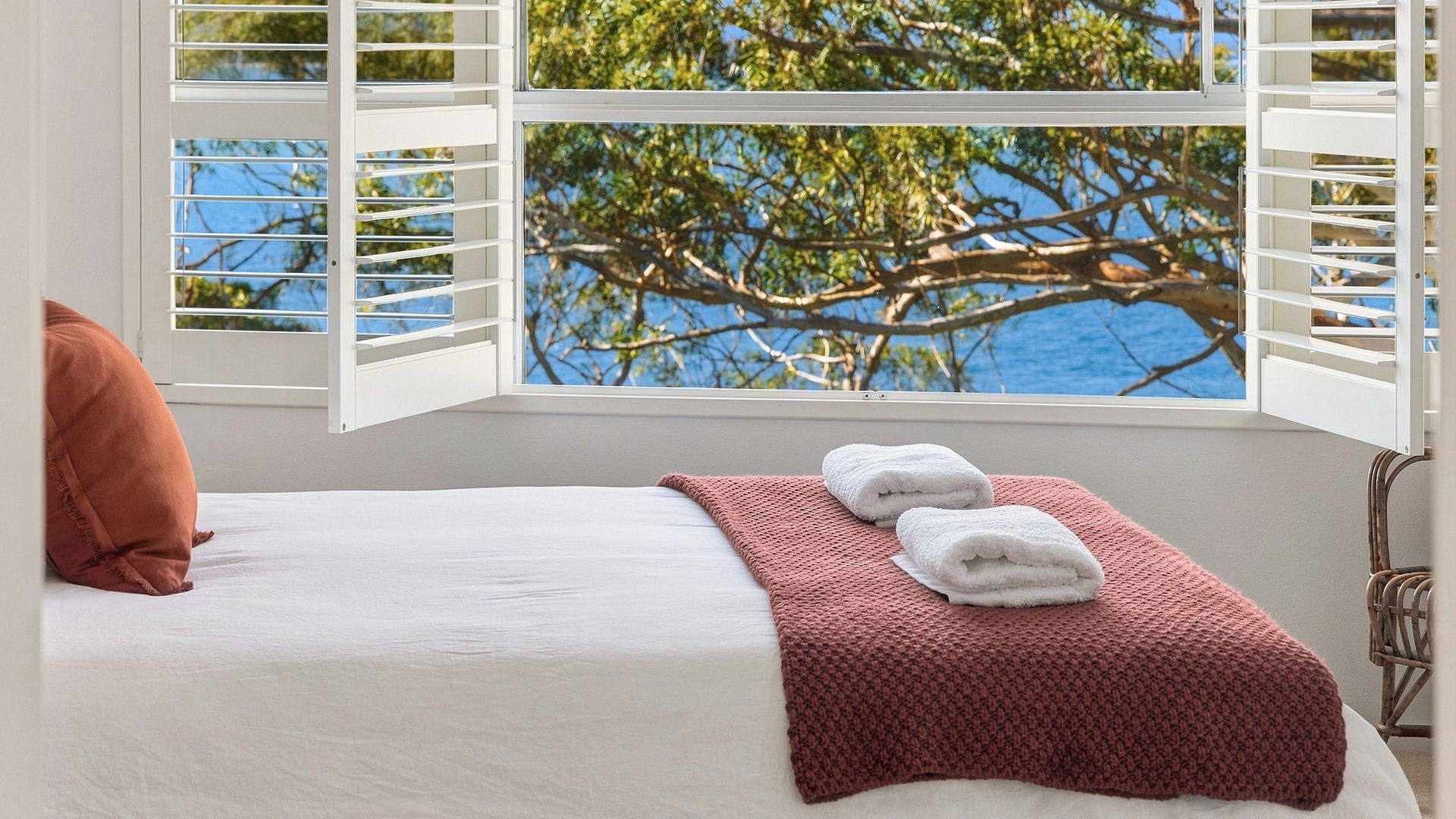 Una cama con ropa blanca, un plaid tejido rojo y dos toallas blancas.