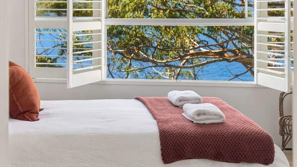 Una cama con ropa blanca, un plaid tejido rojo y dos toallas blancas.