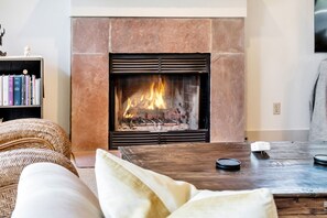 Ein Wohnzimmer mit Kamin, Bücherregal, Rattan-Sofa und Couchtisch aus Holz.