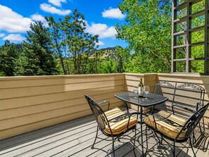 An outdoor patio with a table and chairs, a bottle of wine, and a view of trees and hills. - Peaceful 3BR Retreat in Boulder | Mountain Views (Boulder)