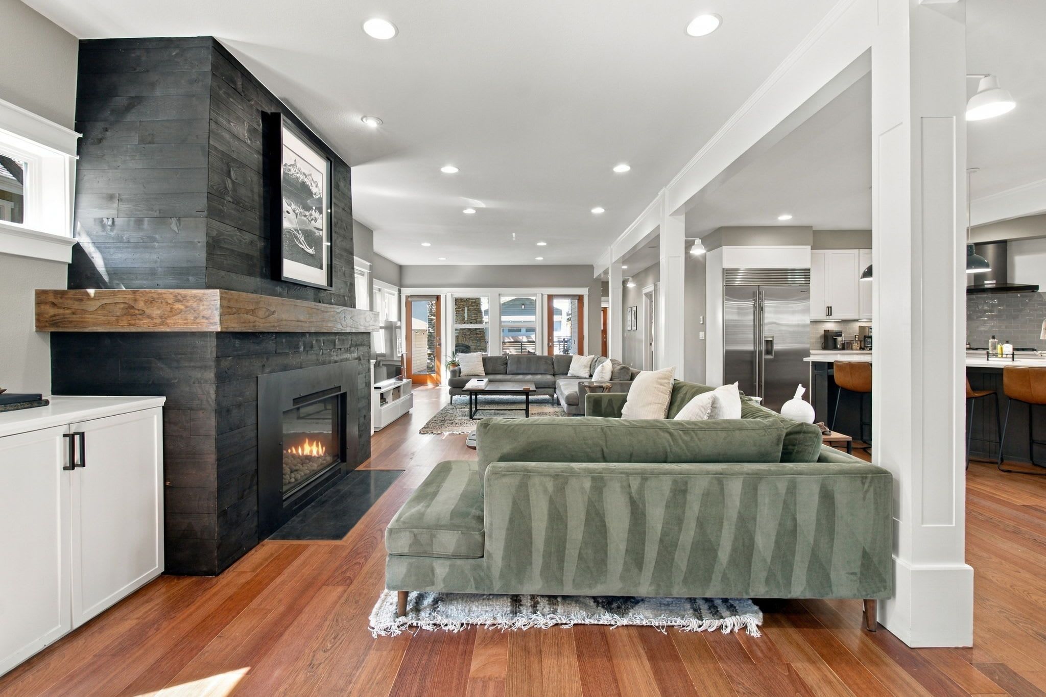 A modern living room with a fireplace, a green sofa, and a kitchen in the background.