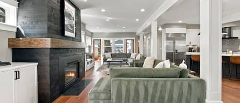 A modern living room with a fireplace, a green sofa, and a kitchen in the background.