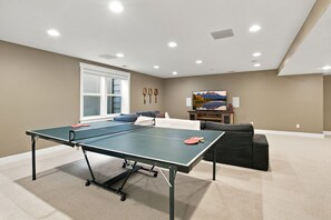 A room with a ping pong table, a sofa, a TV, and a window. - Boulder Luxury | Stunning 6BR on Boulder Foothills (Boulder)