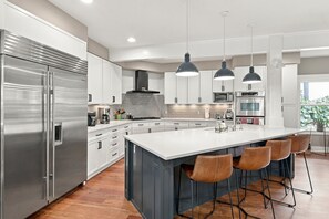 A modern kitchen with a large island, stainless steel appliances, and pendant lighting.